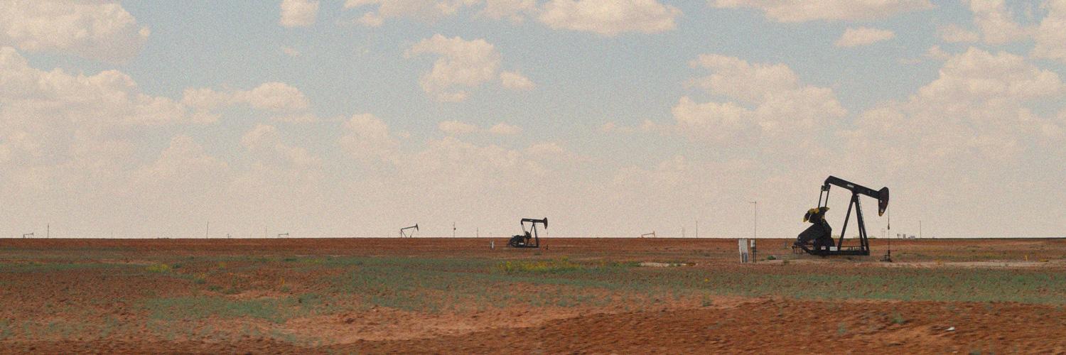 Oil pumpjacks operating across a flat, arid Texas landscape beneath a cloudy sky